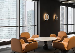 Interior of modern office waiting room with gray walls, concrete floor, orange armchairs standing near round coffee table and conference room in background. 3d rendering